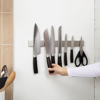 Set of knives and scissors on a apampvanna's magnetic strip against a white wall.