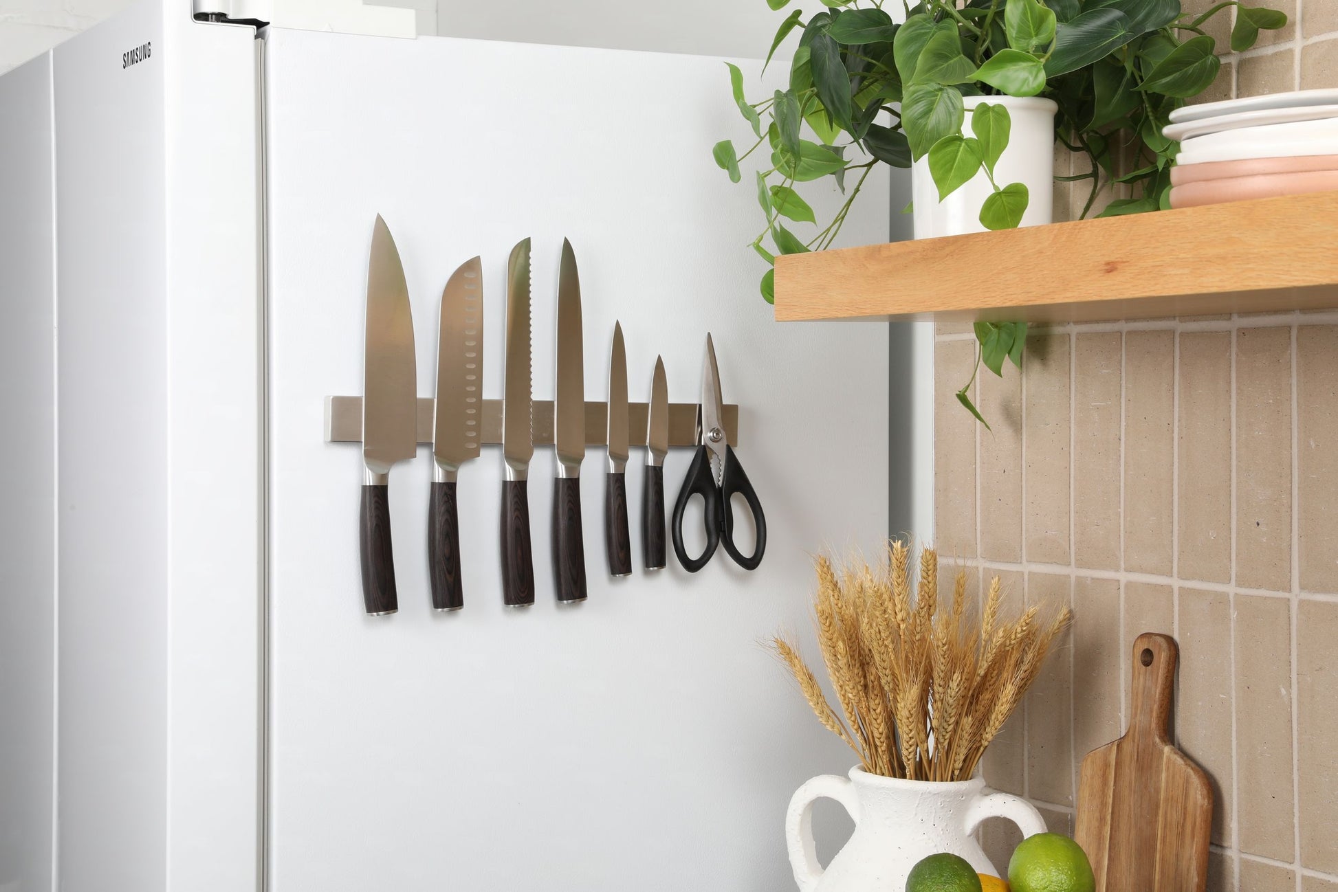 Kitchen scene with knives, scissors, and a cutting board on a magnetic strip against a white wall.